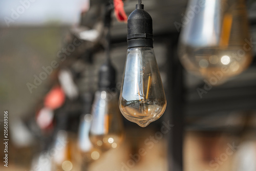 Close up of vintage Edison string lights hanging outdoors during daytime. Decorative unlit patio illumination with shallow depth of field in Latvia.