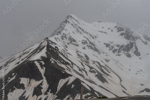 Photography Picturesque Grossglockner High Alpine Road in Austria surrounded by rugged snowy peaks, green Alpine slopes and dramatic cloudy mountain scenery
