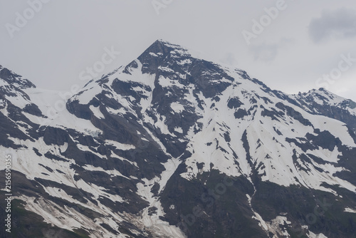 Photography Picturesque Grossglockner High Alpine Road in Austria surrounded by rugged snowy peaks, green Alpine slopes and dramatic cloudy mountain scenery