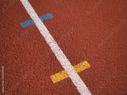 Obraz na płótnie Textured red rubber running track surface featuring solid white lane lines contrasted with smaller blue and yellow markings