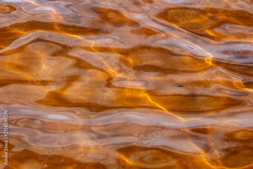 Golden water ripplers on a beach surface. With bright sun reflection. 
