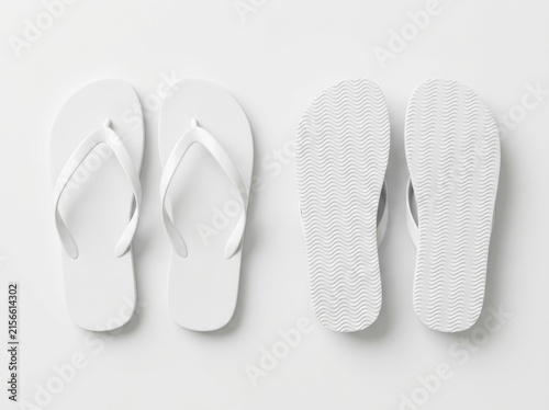 Two pairs of white rubber flip flops with wavy sole pattern lying on white surface