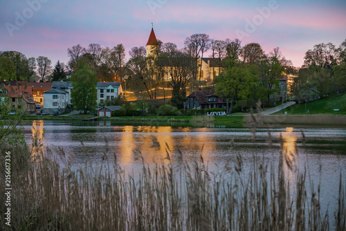 Scenic dawn over Talsi town in Latvia with church and lights reflecting in lake water, view through dry reeds