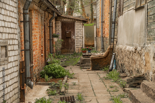 Cozy old courtyard alley between brick and wooden buildings with plants and vintage armchair in Talsi, Latvia