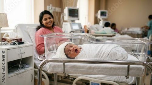 Swaddled infant in a maternity ward with mother in the background