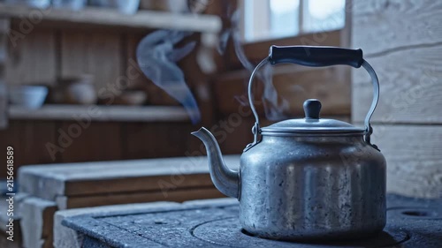 A kettle sits on a stove in a cozy kitchen. Steam rises, showing the kettle is heating water. The wooden shelves and rustic decor add to the homey feel