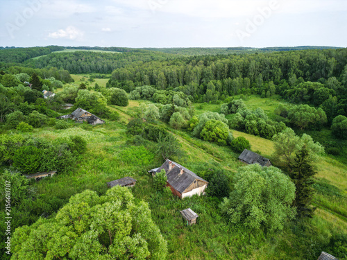 Abandoned village surrounded by dense forest. Atmospheric rural landscape featuring deserted houses, overgrown vegetation, and signs of a forgotten settlement.