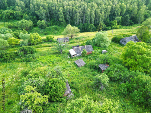 Abandoned village surrounded by dense forest. Atmospheric rural landscape featuring deserted houses, overgrown vegetation, and signs of a forgotten settlement.
