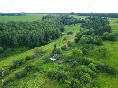 Abandoned village surrounded by dense forest. Atmospheric rural landscape featuring deserted houses, overgrown vegetation, and signs of a forgotten settlement.