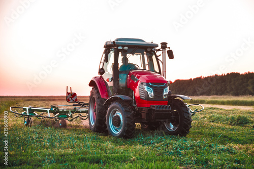 Modern red tractor working with forage harvesting equipment in an agricultural field. Contemporary farm machinery used for efficient hay and forage production.