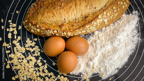 Foto Oatmeal bread, three chicken eggs, and wheat flour are laid out on a kitchen mat