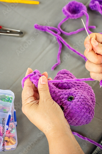 Hands sewing purple plush crochet amigurumi toy with needle and yarn in craft process