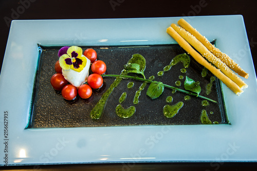 Food Photography art shots, white Cheese surrounded by charry tomatoes with watercress and green sauce making a flower shape, Caprese, Photo is selective focus with shallow depth of field. Cairo Egypt