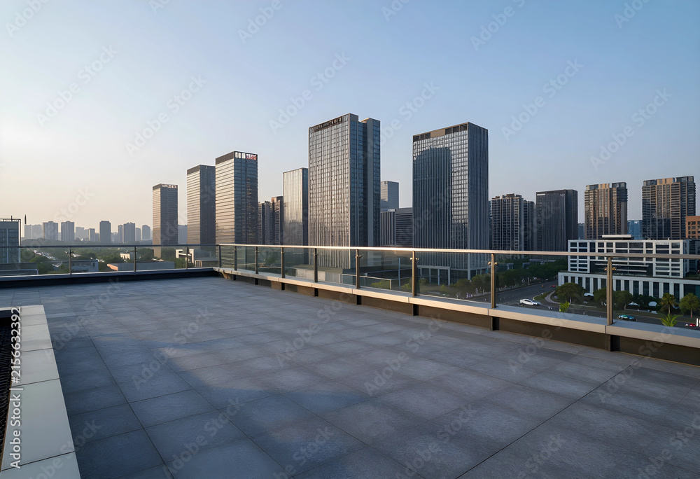 Fototapeta premium Empty rooftop terrace with modern glass railing overlooking a contemporary urban skyline at sunrise, Tall commercial and residential buildings rise against a clear morning sky, illuminated