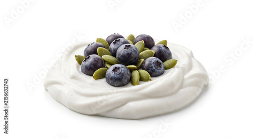 Distant shot of 5 to 10 acai berries and pumpkin seeds resting on thick white cashew vegan yogurt