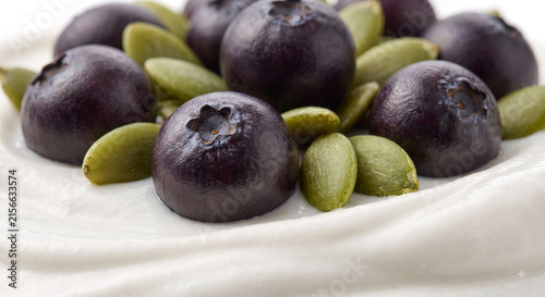 Distant shot of 5 to 10 acai berries and pumpkin seeds resting on thick white cashew vegan yogurt