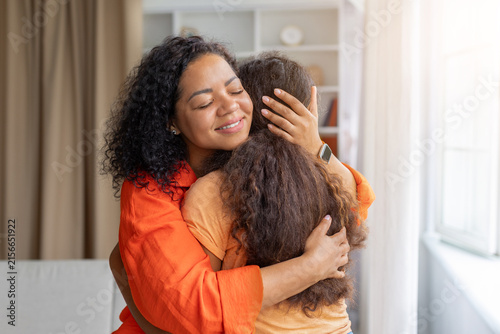 Foto Smiling Black mother embraces her young daughter at home, gently holding her clo