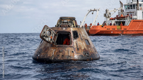 Space capsule re-entry with open hatch floating in ocean near recovery ship