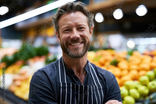 Happy merchant in apron at modern grocery store