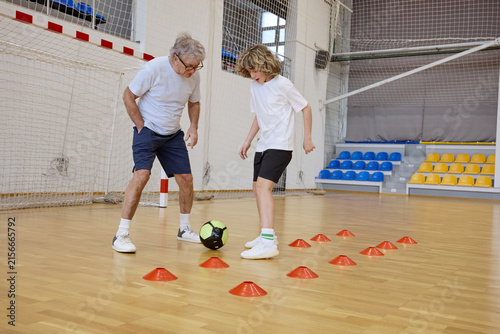 Obraz na plátně Senior man and teenage boy dribbling ball while enjoying an active day at a spor