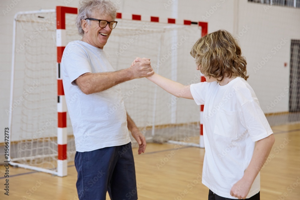 Fototapeta premium Senior man and teenage boy shaking hands while spending time together at an indoor gym