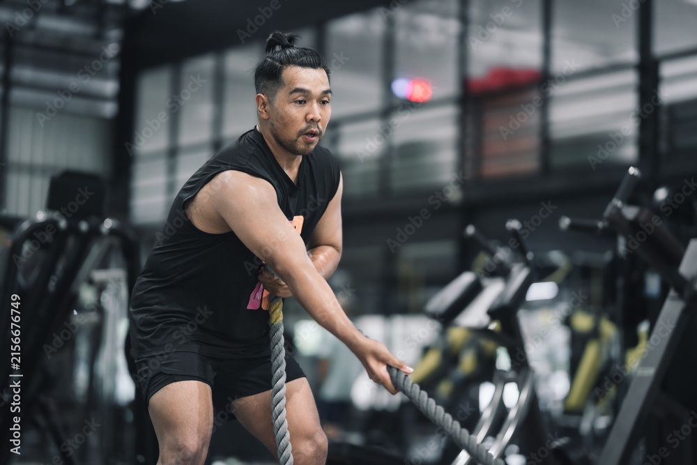 Fototapeta premium Man performing battle rope exercise or exercise with sled pull in gym