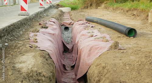 Road construction new sewer pipe drainage installation roadway roadwork, long trench excavated channel, excavation site preparation road repair gravel bedding and geotextile fabric, corrugated pipe