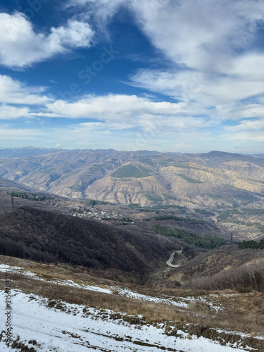 Mountain landscape with winding road and snow patches under bright blue sky.