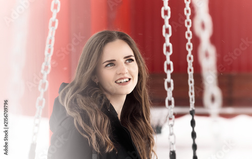 Smiling young woman at a snowy playground surrounded by swing chains. Warm winter lifestyle portrait with soft light, happiness and outdoor leisure concept.
