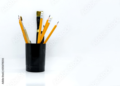 Yellow pencils and paint brushes in black holder on white background. Isolated art supplies for creativity, drawing, painting and education concept design.