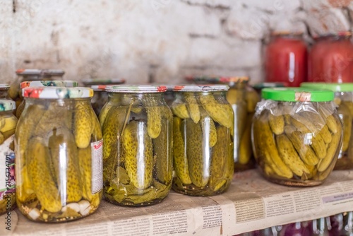 Glass jars filled with pickled cucumbers on pantry shelf close up