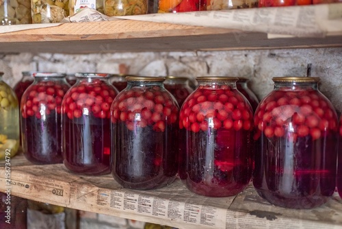 Large glass jars with homemade sweet cherry compote on pantry shelf