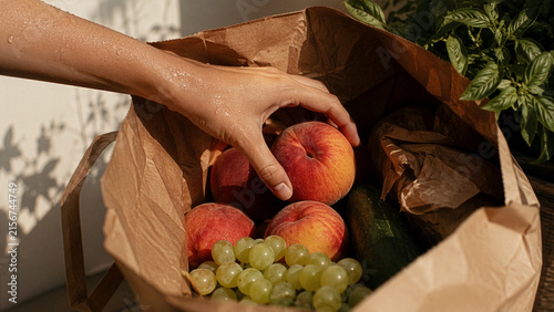Hand Reaching for Fresh Peaches and Grapes in Paper Grocery Bag