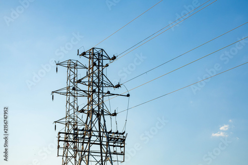 Heavy dead-end electrical transmission towers with power lines plunging vertically downward toward a substation or underground cable against a clear blue sky.