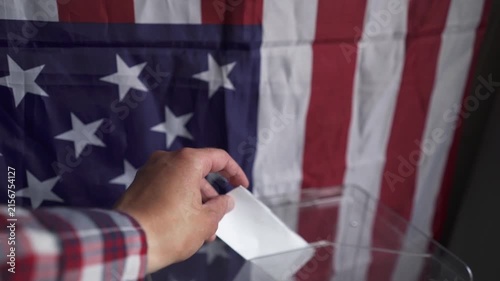 POV of citizen walking up and dropping folded ballot into box with US flag background