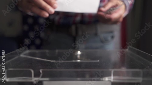 Voter walking up and inserting ballot into slot of transparent box, front view
