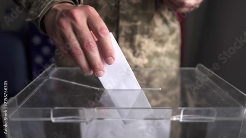 US soldier in camouflage moving and inserting ballot into box, American flag background