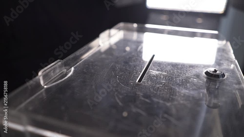 Voter putting ballot sheet into slot of transparent box close up during elections