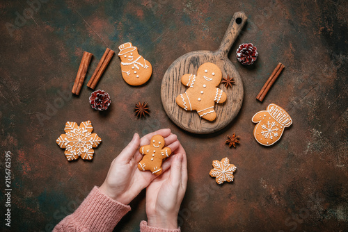 Female hands holding gingerbread man on dark grunge table, Christmas various gingerbread cookies, top view, flat lay.