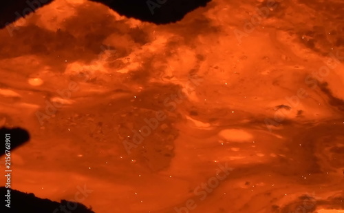 Foto A vivid close-up of a cylindrical refractory structure surrounded by glowing molten material, showing bright orange heat, scattered sparks, and dynamic fluid motion within an industrial furnace