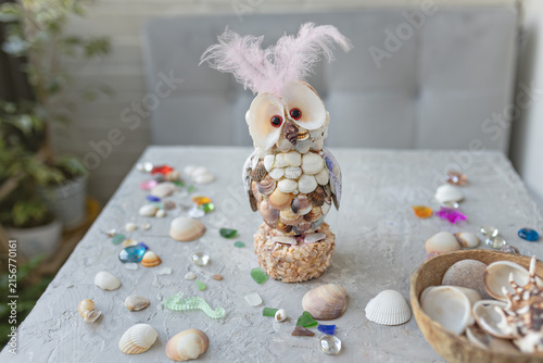 Owl figurine made of seashells with pink feathers on gray table
