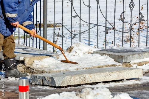 Worker removes snow from sidewalk in winter near a decorative fence
