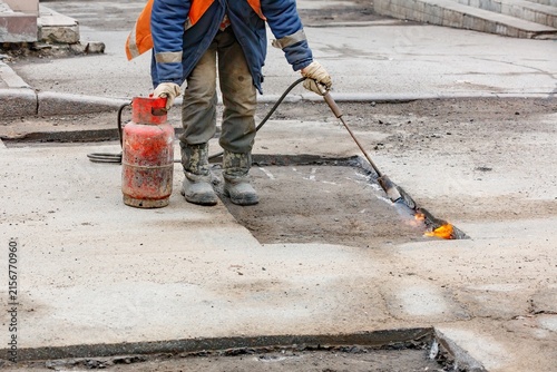 Worker repairs road with torch and fire on street in urban area during the day