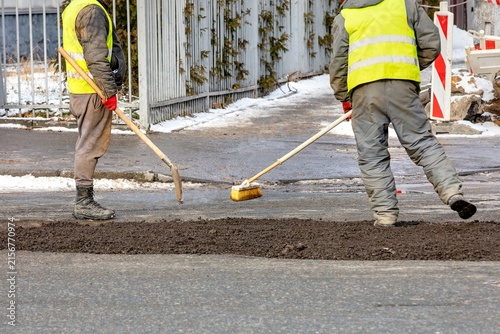 Workers repair a road in a city during daylight hours with tools and equipment