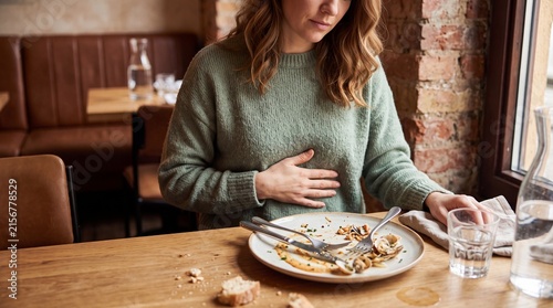 Stomach ache and indigestion after eating, woman holding bloated belly in restaurant, food intolerance and digestive health concept