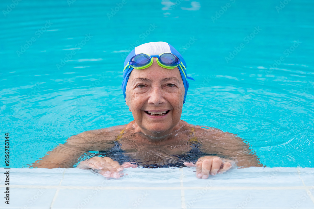 Fototapeta premium Happy senior woman enjoying a refreshing swim in a bright blue pool, wearing a swim cap and goggles, actively engaging in a healthy, active lifestyle and wellness