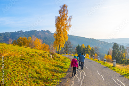 People walk along a road surrounded by autumn trees in Albrechtice, located in the Jizera Mountains, Czechia. The colorful leaves mark the change of the seasons.
