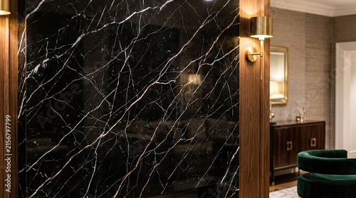 A luxurious marble wall with dark and light shades, framed by wooden columns and a mirror, in a modern living room with green and black furniture.