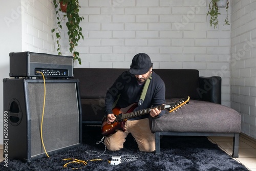 Canvas Print Full shot of man with electric guitar tweaking audio effect pedal on floor durin