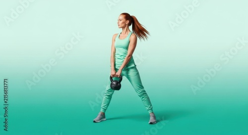 Athletic Woman in Mint Green Activewear Lifting Kettlebell in Studio